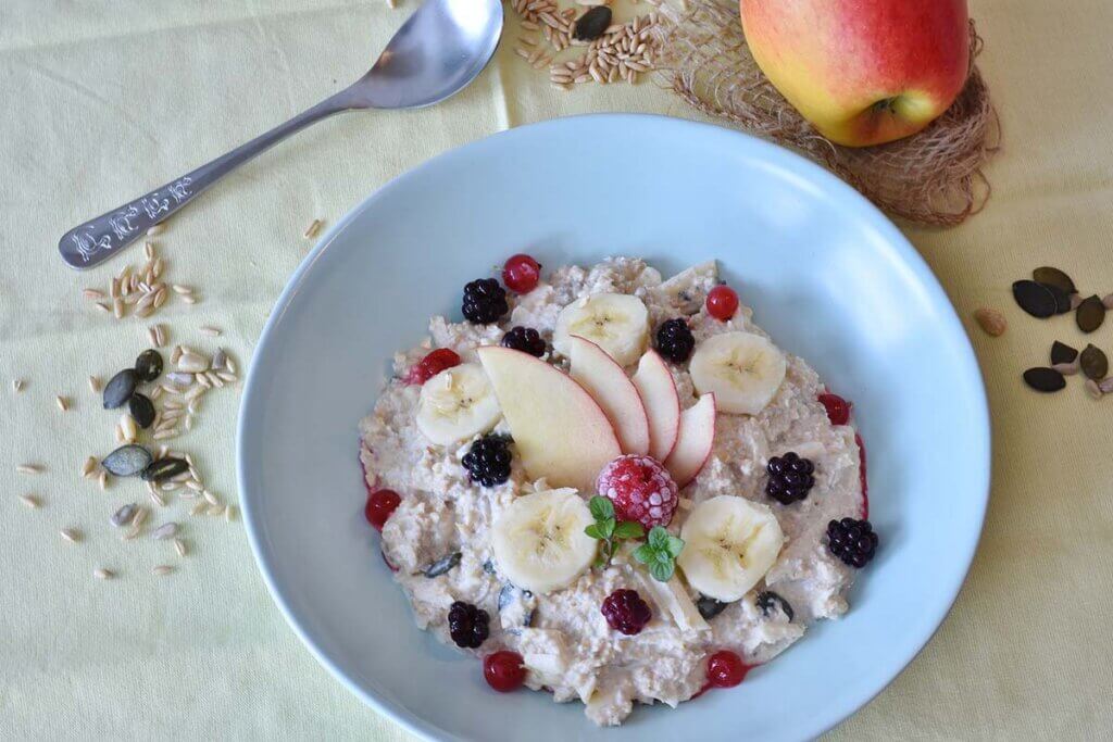 Ein Porridge mit Bananen und Beeren dekoriert, als veganes Fruehstueck.