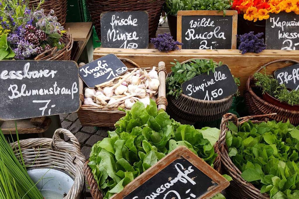 Ein Stand auf einem Markt, mit vielen Salaten und Blumen in Koerben.