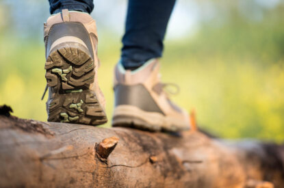 Person mit schwarzer Hose und beigen Wanderschuhen laeuft ueber einen Baumstamm.