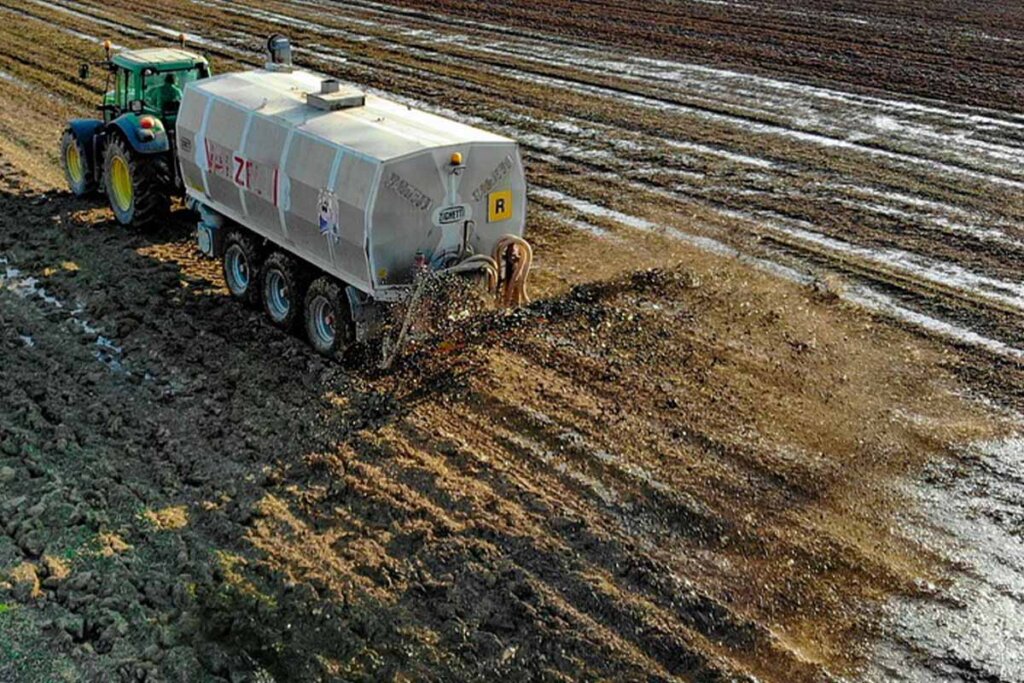 Ein Traktor mit Anhaenger faehrt auf einem Acker und verteilt Guelle.