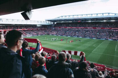 Fans im Fussballstadion schauen ein Spiel an und halten Schals in die Hoehe.