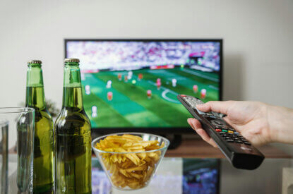 Im Fernseher läuft Fußball und auf dem Tisch steht Bier und Chips